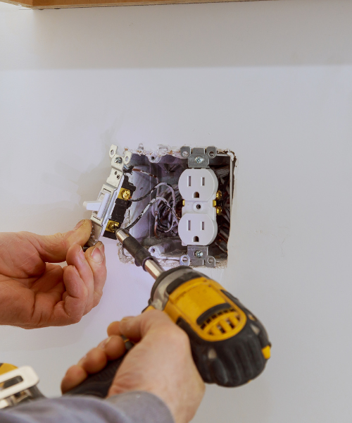 A person using a drill to fix a light switch