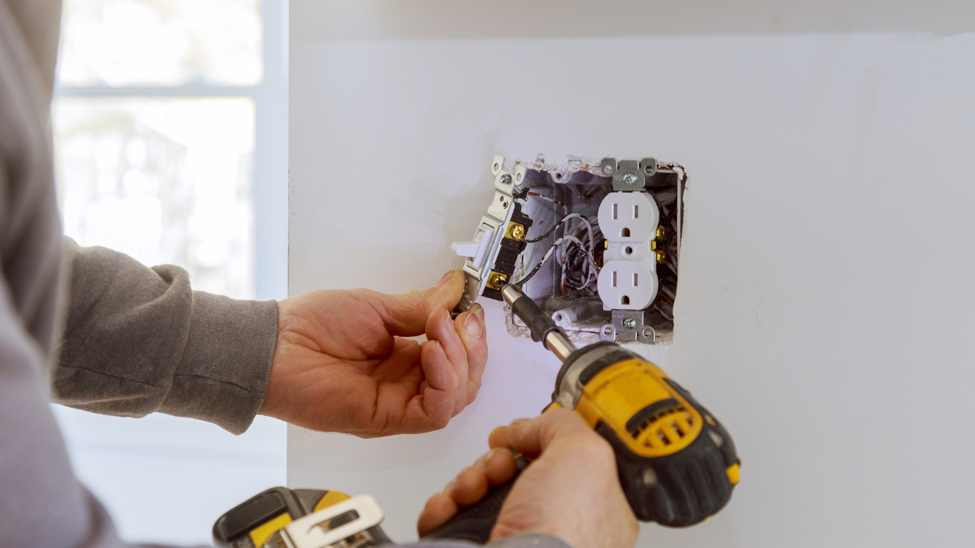 A man is using a screwdriver to fix a light switch